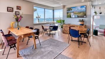 A modern dining area with a wooden table, chairs, and a view of the sea.