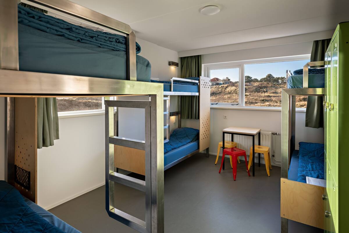 Una habitación compacta con literas, una mesita pequeña y una ventana con vistas a un paisaje montañoso.