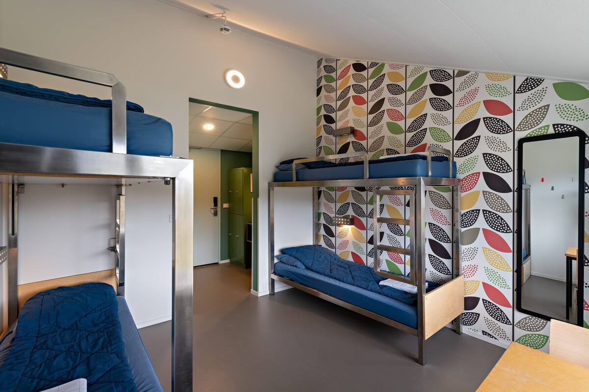 Habitación con literas, una pared con estampado de hojas de colores, una mesa de madera y un espejo.