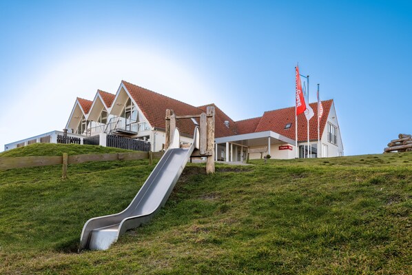 A building with a red-tiled roof, a wooden fence, and a metal slide. - Stayokay Terschelling - Hostel (West-Terschelling)
