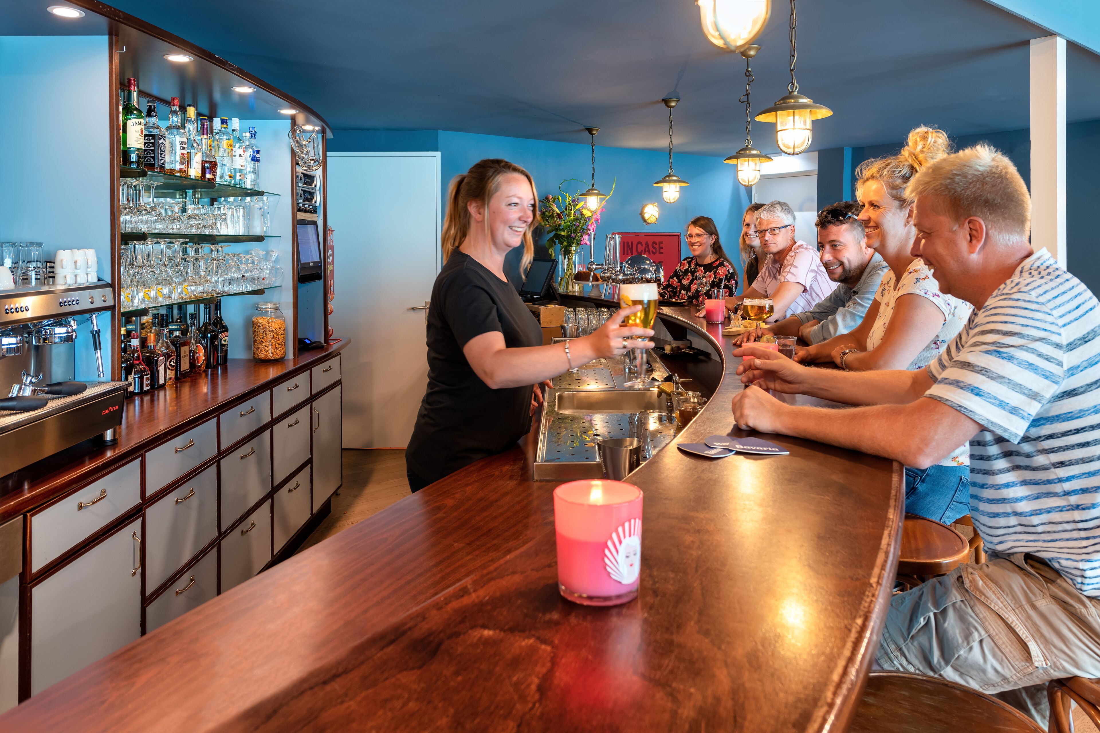 A bar area with a bartender serving drinks to a group of people seated at a wooden table.