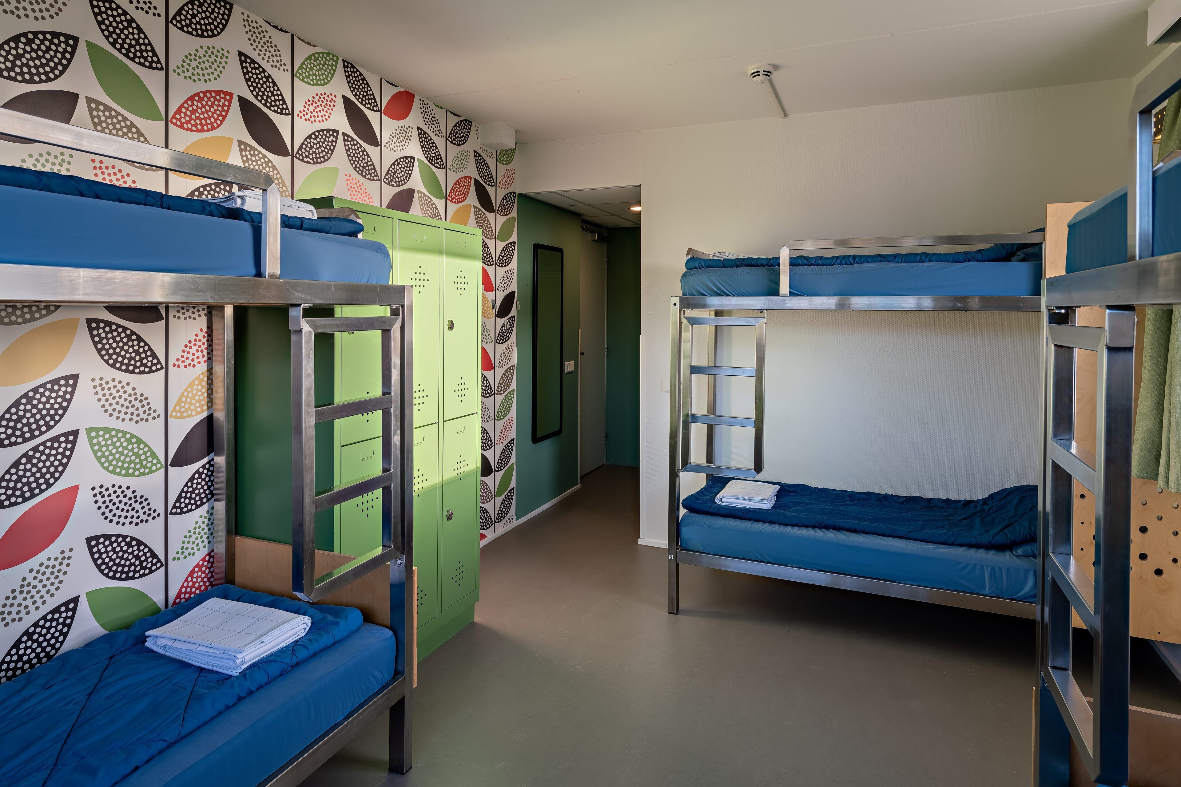 Ein Schlafsaalzimmer mit Etagenbetten, Schließfächern und einer Wand mit Muster.