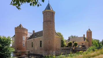 Un edificio histórico de ladrillo con una torre destacada y una torreón más pequeño, ubicado junto a un canal.