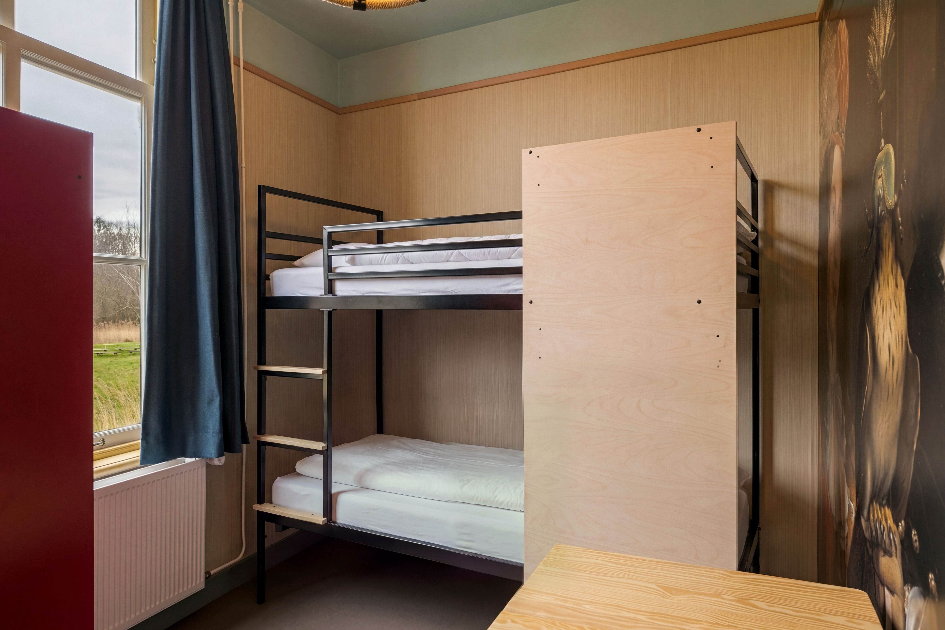 Een slaapkamer met een stapelbed, een houten hoofdbord, een klein houten tafeltje en uitzicht op de omgeving door een raam.