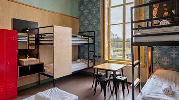 A dormitory room with bunk beds, a desk, a chair, a red wardrobe, and a window with a view.