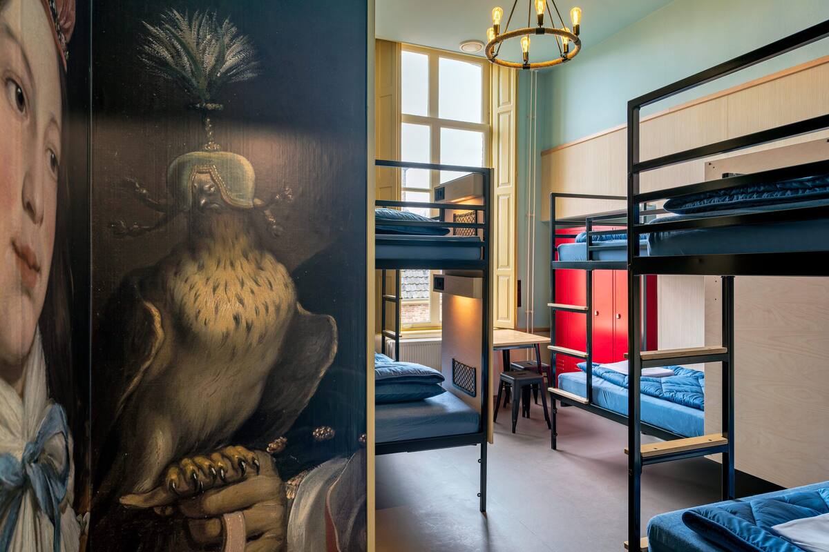 Een kamer met stapelbedden, een bureau en een stoel. Er is een raam waardoor daglicht schijnt.