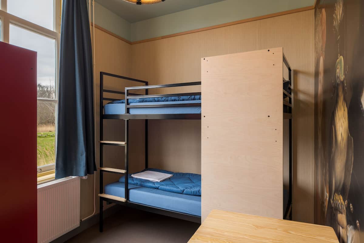 Een slaapkamer met een stapelbed, een raam, een radiator en een houten bureau.