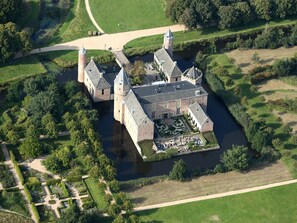 Vista aérea de un edificio histórico con un patio central, rodeado de abundante vegetación y un río.