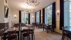 A spacious dining area with multiple tables and chairs, large windows with dark curtains, and a chandelier. - Stayokay Utrecht Bunnik - Hostel (Bunnik)