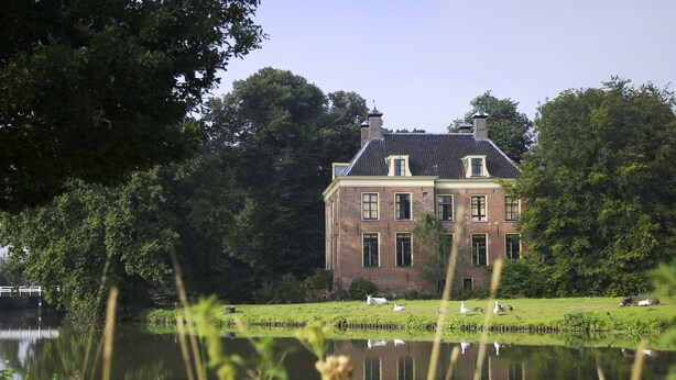 A large brick building with a symmetrical facade, a prominent central chimney, and a reflection in the water in front. - Stayokay Utrecht Bunnik - Hostel (Bunnik)