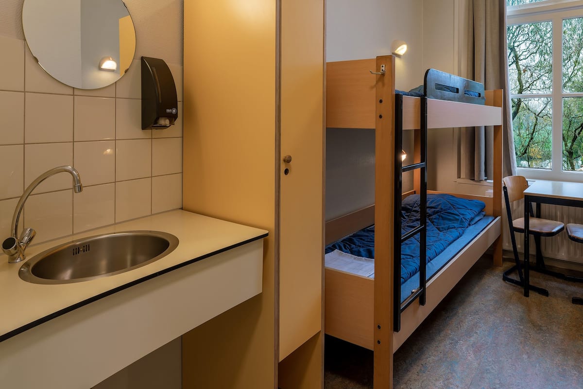 A bunk bed with a desk and chair, a sink, and a window with a view of trees.