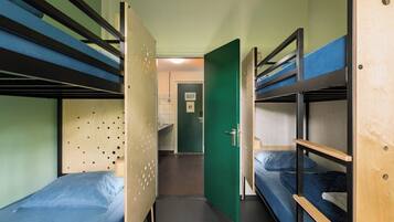 Habitación con literas, una puerta verde, un lavamanos y un ventanal pequeño.