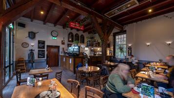 Un restaurant chaleureux avec des tables et des chaises en bois, un coin bar et un tableau affichant le menu.