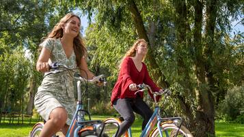 Deux personnes font du vélo dans un parc, entourées d’arbres et d’herbe.
