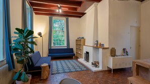 A cozy living room with a blue sofa, a large potted plant, a patterned rug, and a fireplace. - Stayokay Utrecht Bunnik - Hostel (Bunnik)