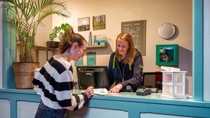 A reception desk with a computer, a plant, and a menu board. - Stayokay Utrecht Bunnik - Hostel (Bunnik)
