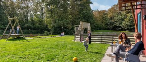 Een terras met buitenmeubels, een schommel en een kleine speelconstructie.