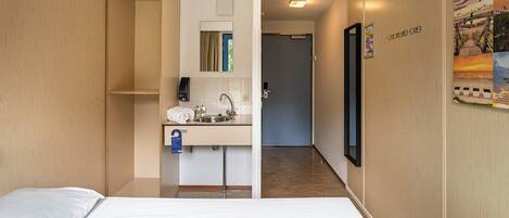 A hotel room with a bed, a bathroom with a sink, and a mirror.
