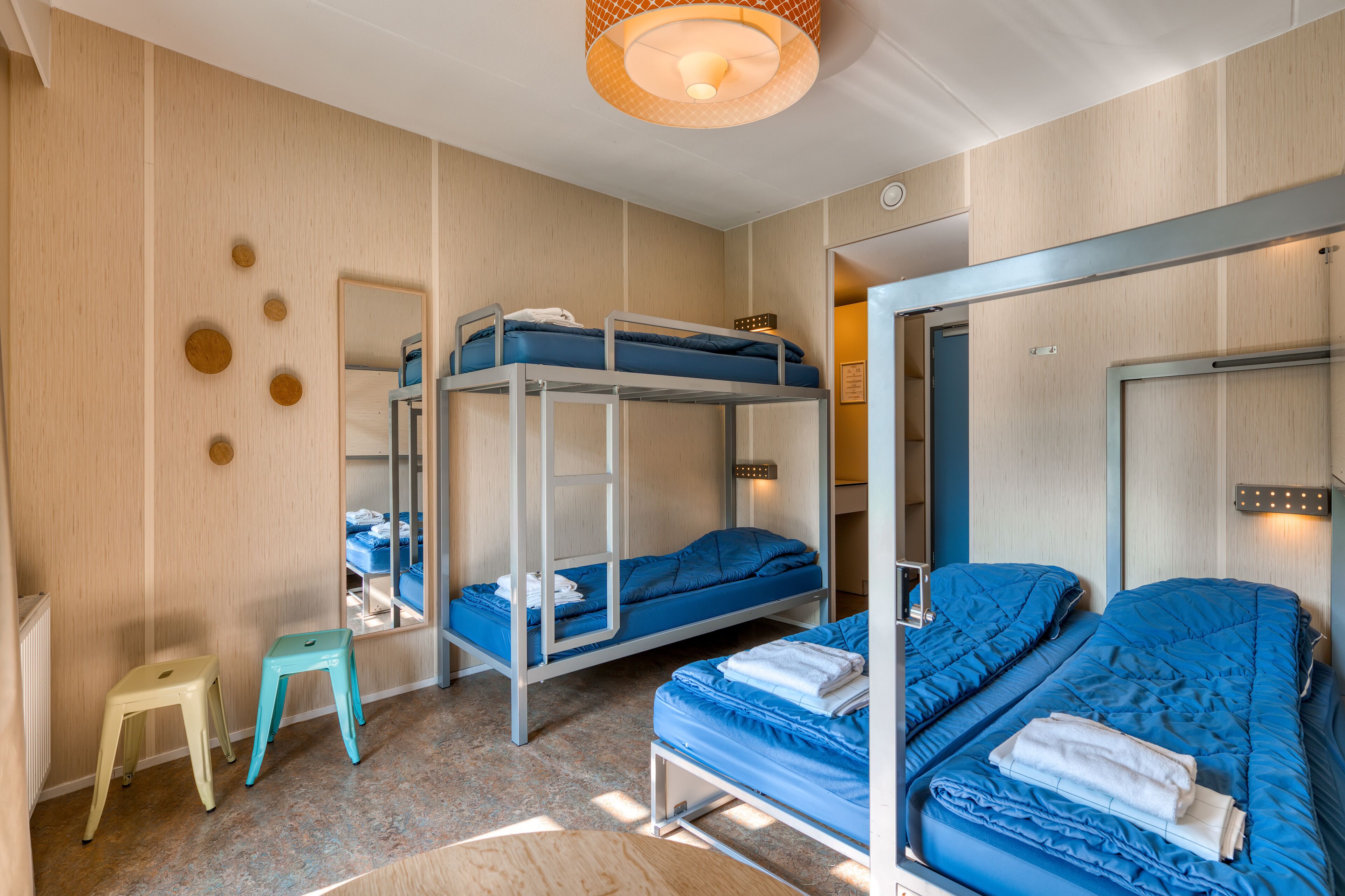 A bunk bed room with a mirror, two stools, and a ceiling light fixture.
