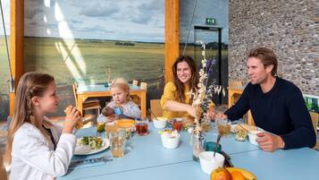 A family dining at a table with a view of a field, a stone wall, and a wooden ceiling.