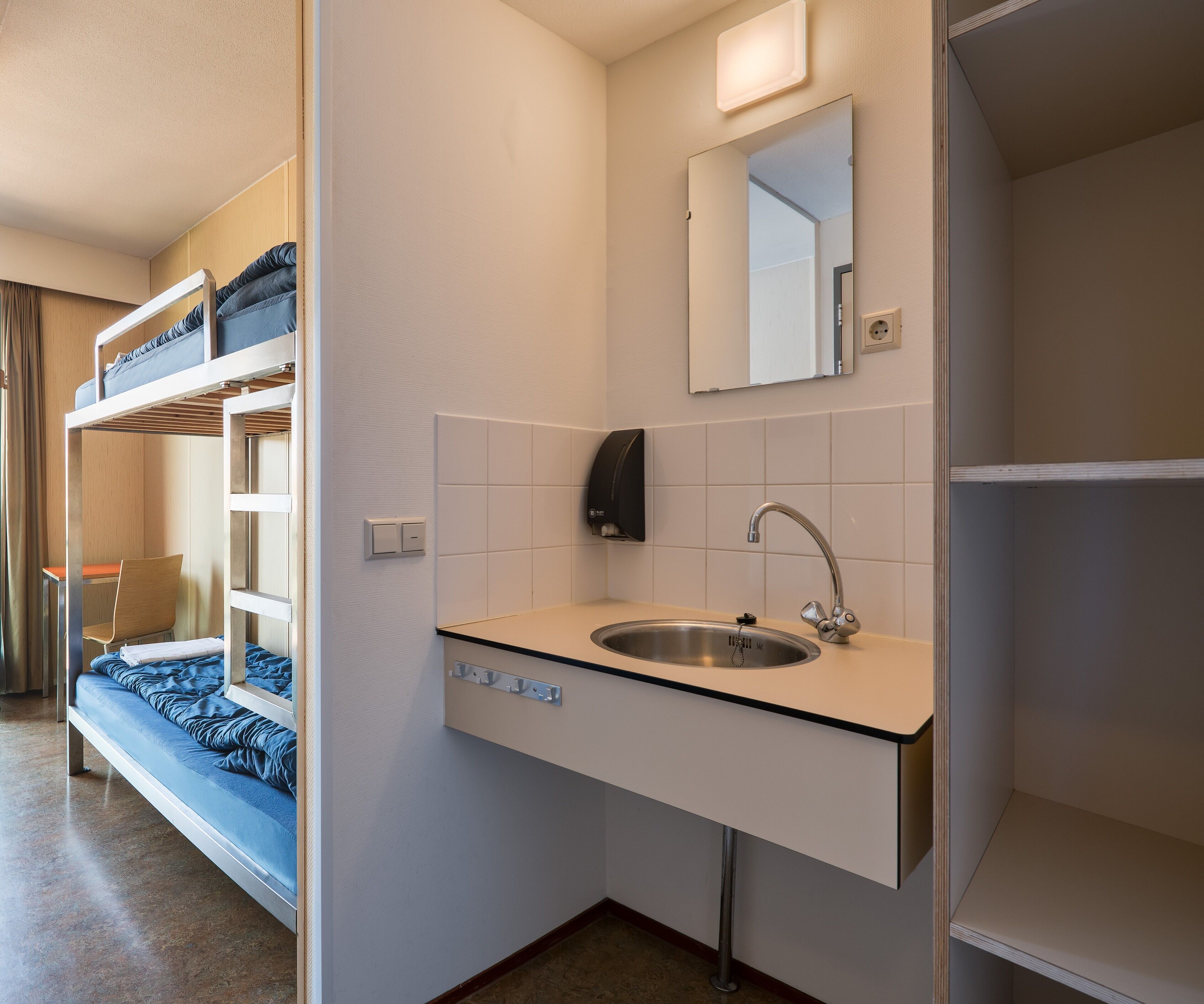 A compact hotel room with a bunk bed, a sink, and a mirror.