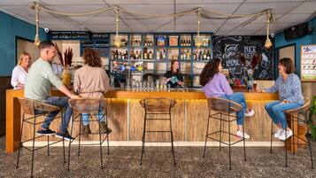 A bar area with wooden stools, a bar counter, and a variety of bottles and glasses.