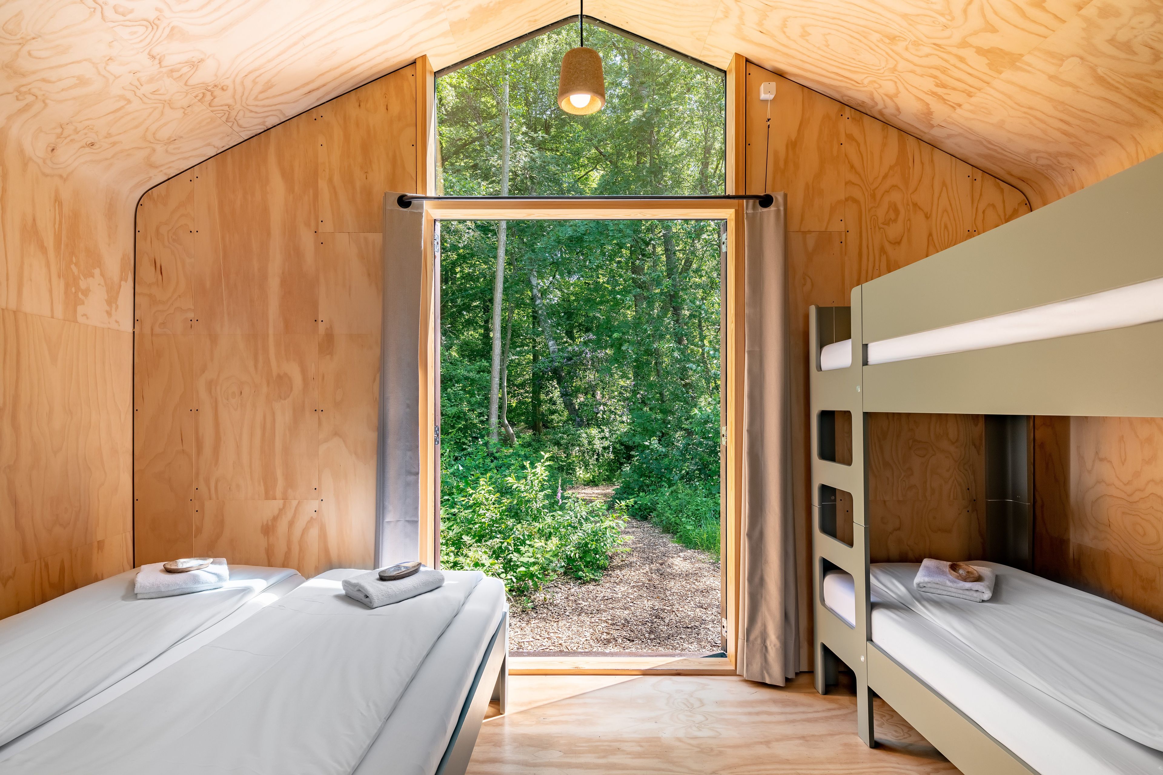 A wooden cabin with two bunk beds, a large window, and a view of a forest.