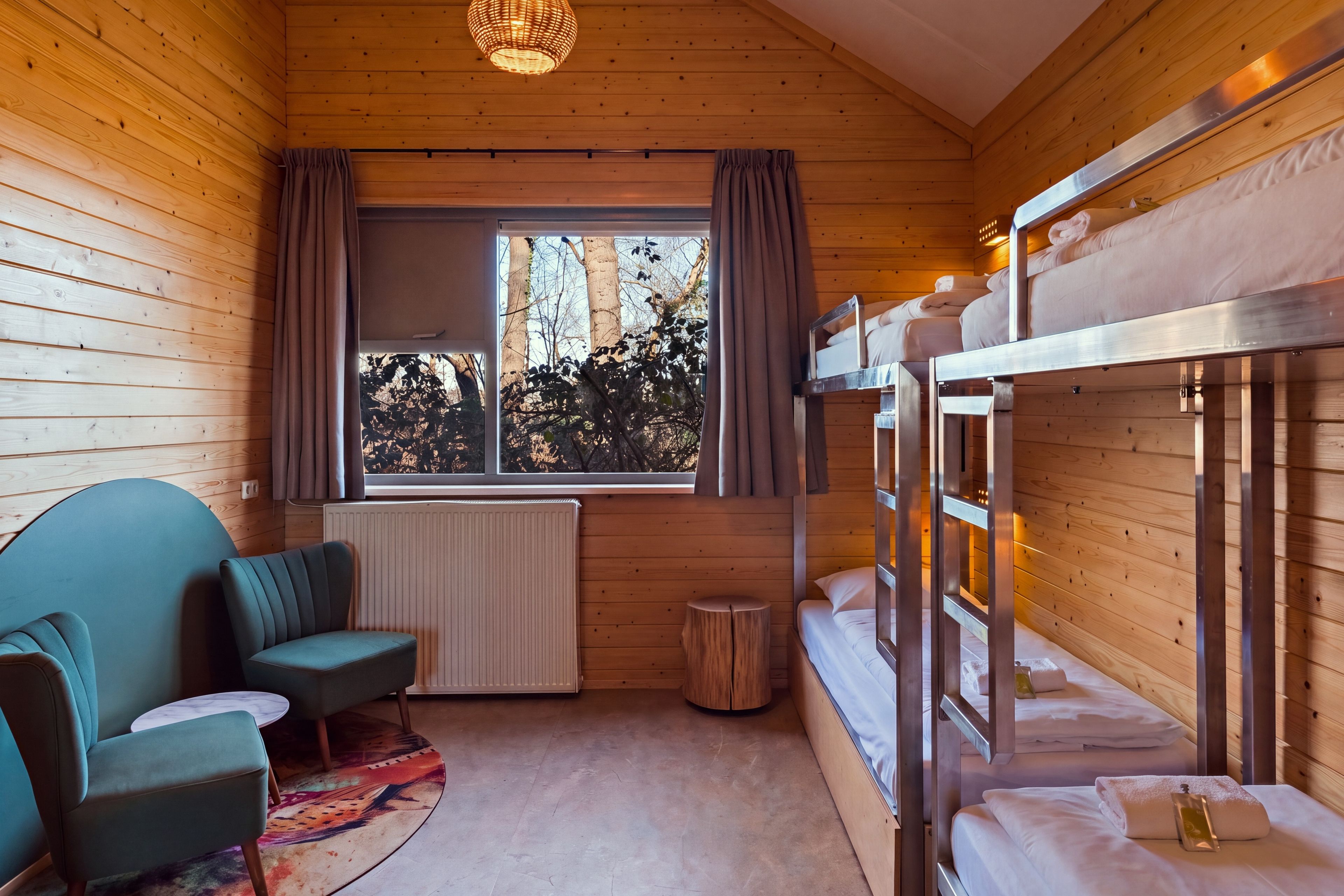 Una habitación tipo cabaña de madera con literas, un sofá, una mesita y una ventana con cortinas.