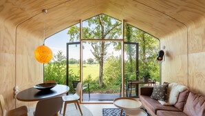 Un espacio habitable moderno y abierto con un amplio ventanal que da a un jardín, muebles de madera y una zona de estar acogedora.