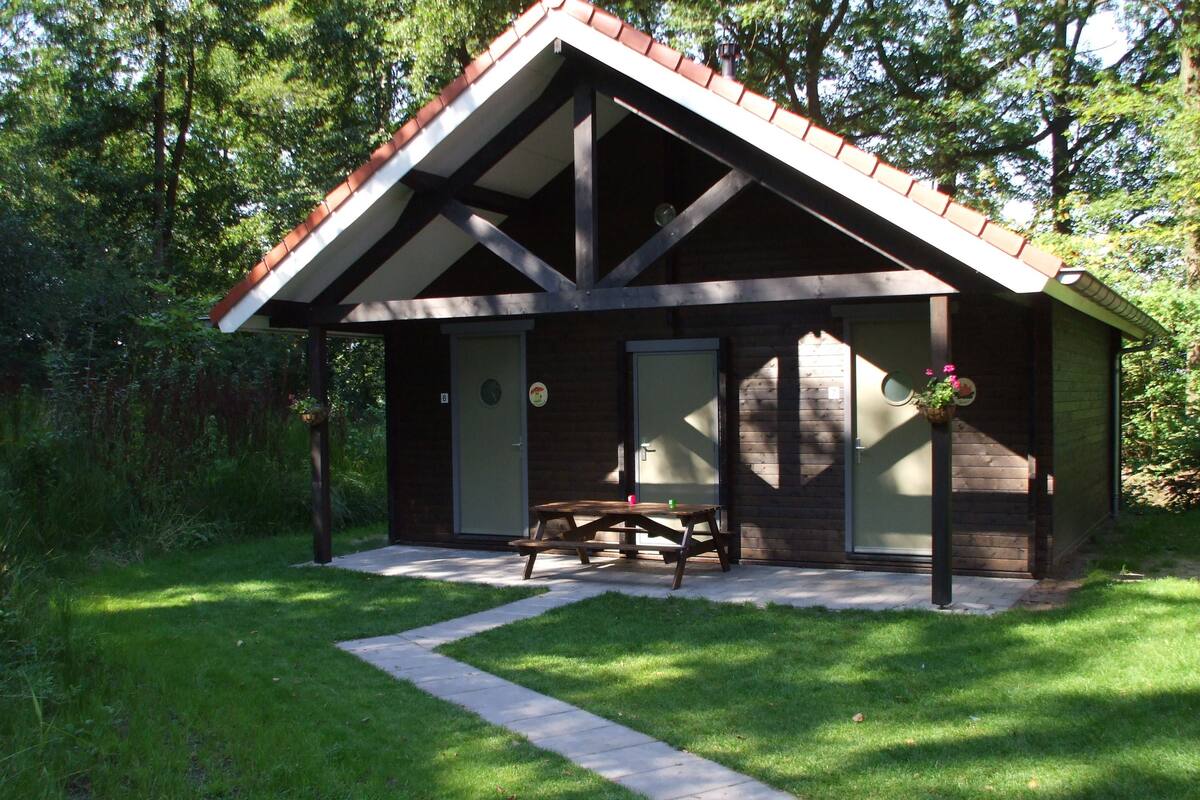 Una cabaña rústica con techo inclinado, una terraza de madera y una mesa de picnic.