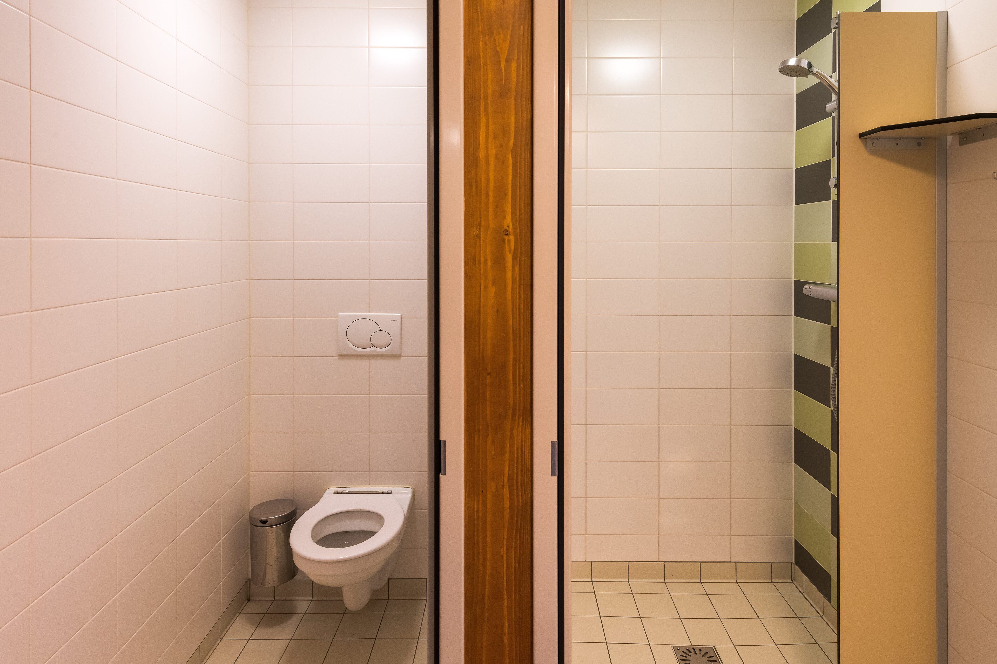 A small, enclosed bathroom with a toilet, a trash can, and a shower area.