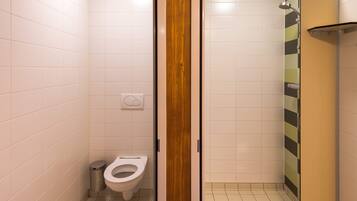Un baño pequeño y cerrado con inodoro, un bote de basura y zona de ducha.