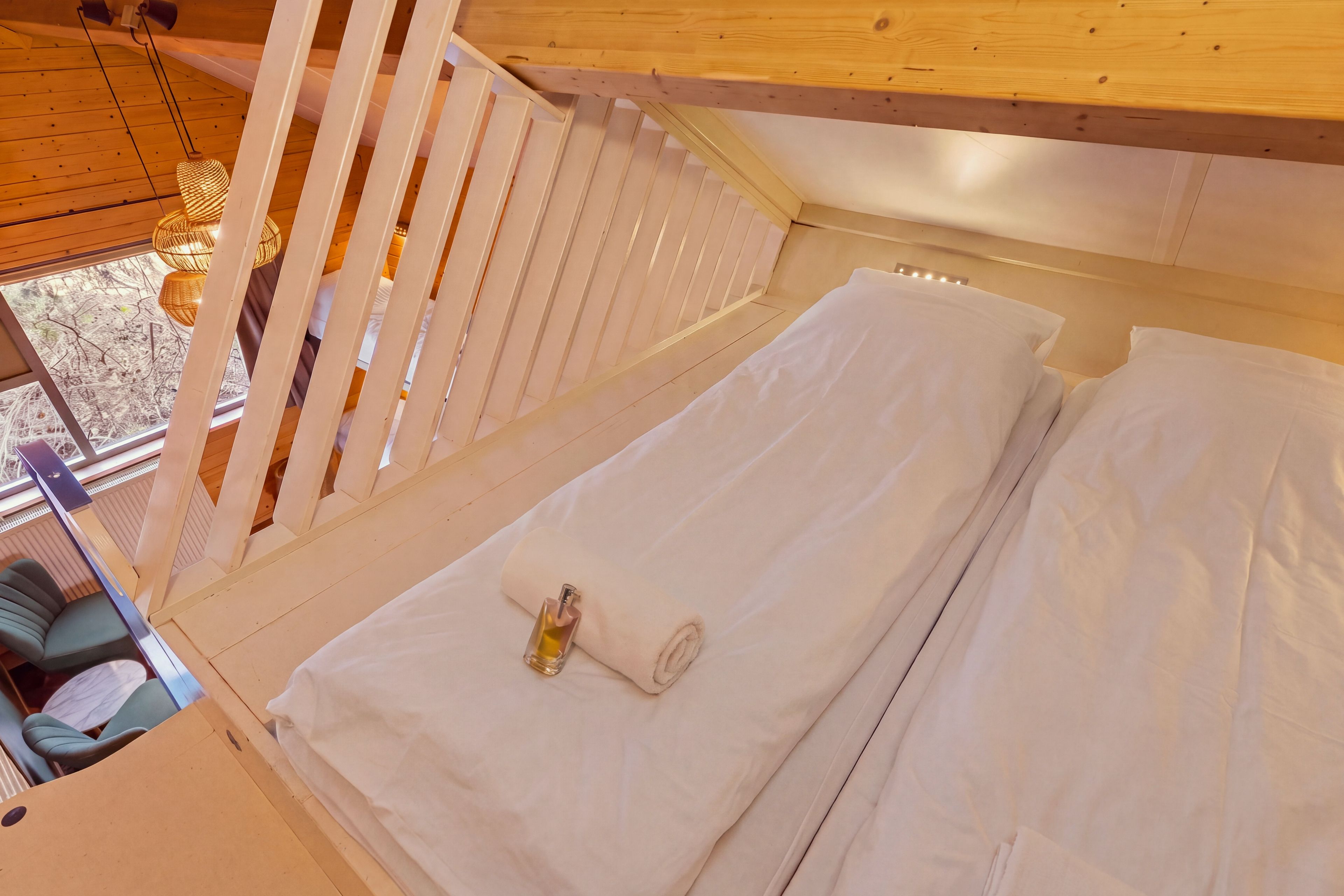 A bed with white linens, a rolled towel, and a bottle of lotion.