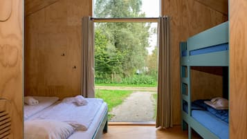 Ein Holzinnenraum mit einem Bett, einem Etagenbett und Blick auf eine grüne Landschaft durch eine offene Tür.