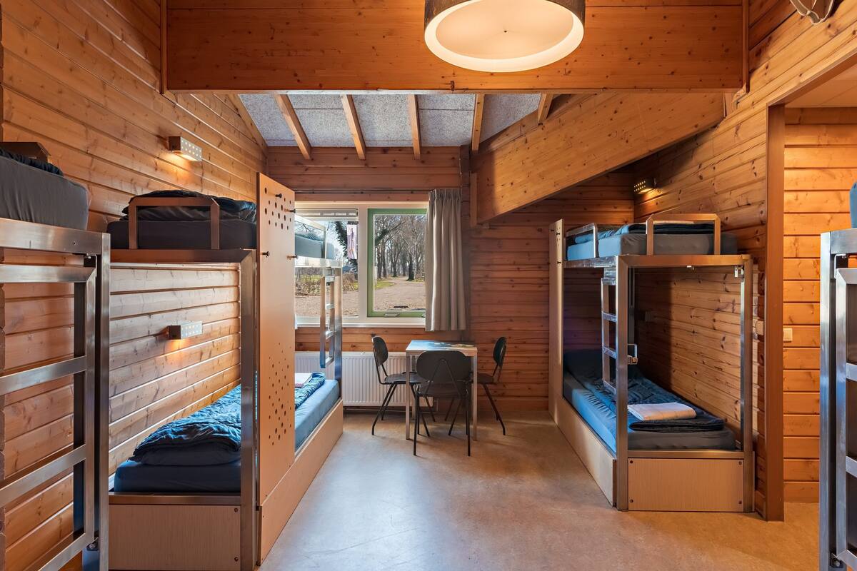 Een compacte hut met stapelbedden, een klein tafeltje en een raam met uitzicht op de natuur.