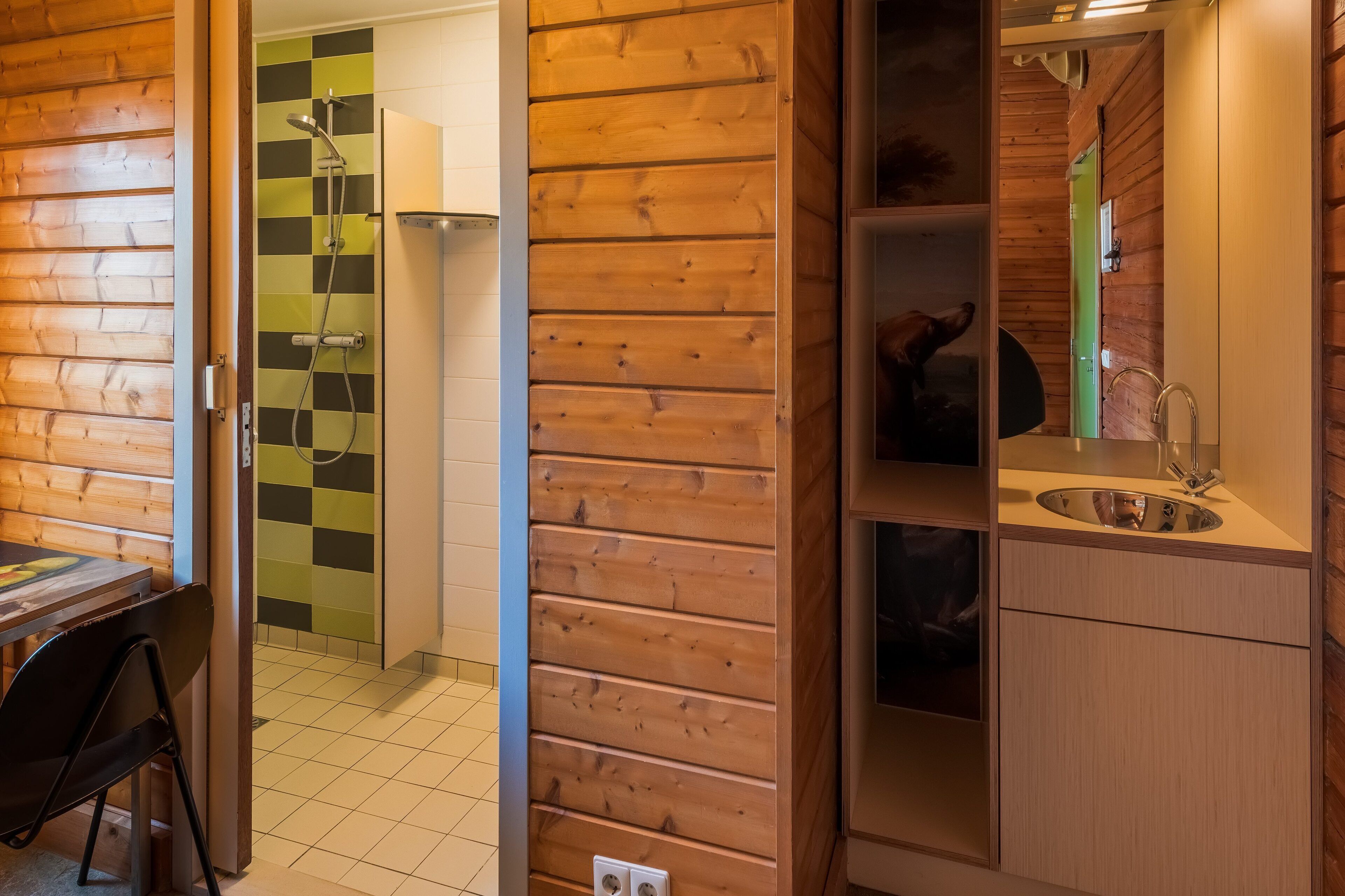 Interior de una cabaña de madera con baño que incluye ducha, lavabo y espejo.