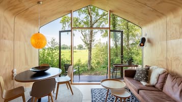 A modern interior with a large glass door leading to an outdoor view, a round dining table, a sofa, and a hanging light fixture.