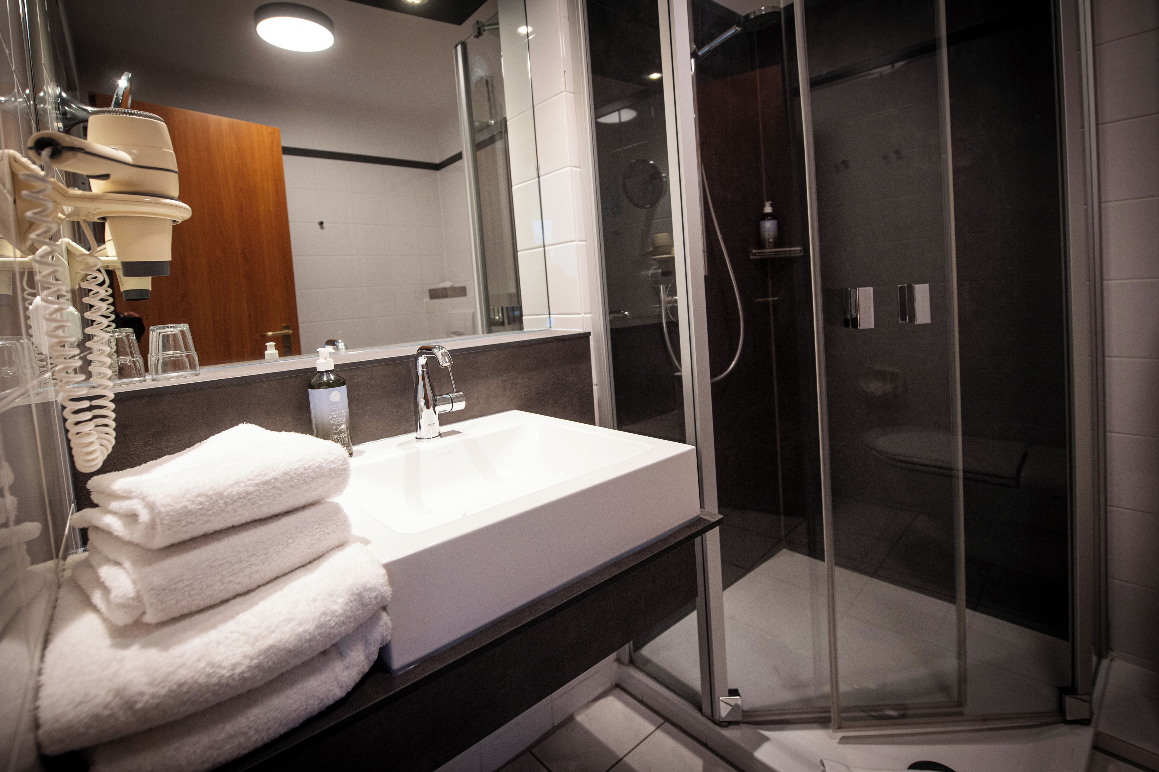 Un baño moderno con lavamanos blanco, cabina de ducha de vidrio y pared de panel de madera.