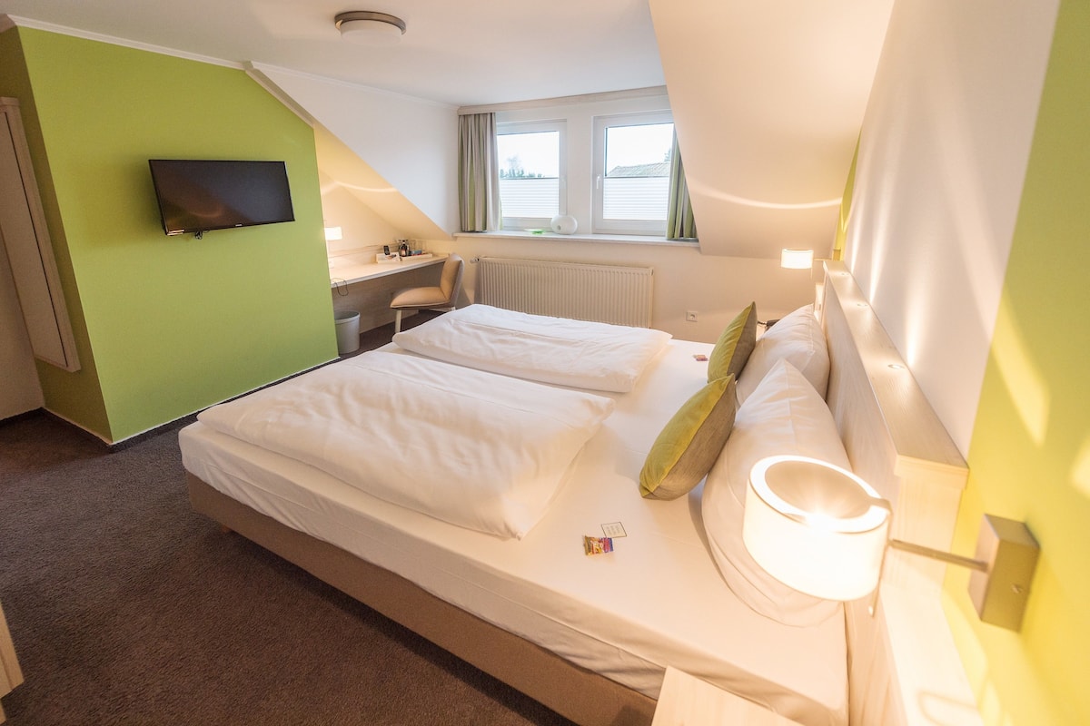 A hotel room with a bed, a desk, a chair, a TV, and a window with curtains.