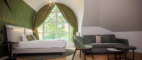 A bedroom with a bed, a sofa, a chair, a small table, and a window with curtains.