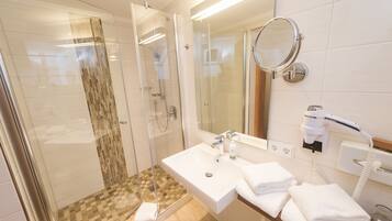 A modern bathroom with a glass-enclosed shower, a white sink with a mirror, and a hairdryer on the countertop.