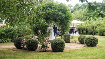 Eine Hochzeitslocation mit Garten, einem zentralen Gang, umgeben von ordentlich geschnittenen Hecken und blühendem Strauchwerk.