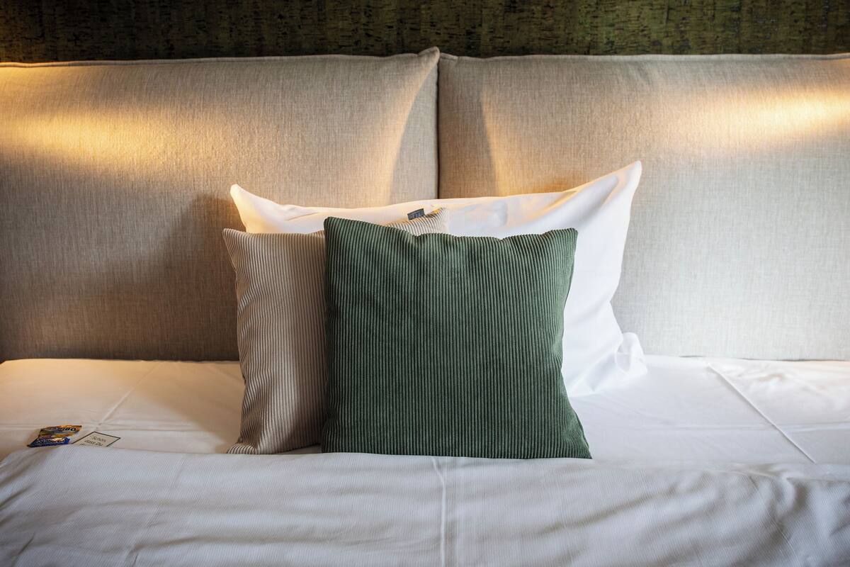 A neatly made bed with white linens and two pillows, one striped and one solid green.