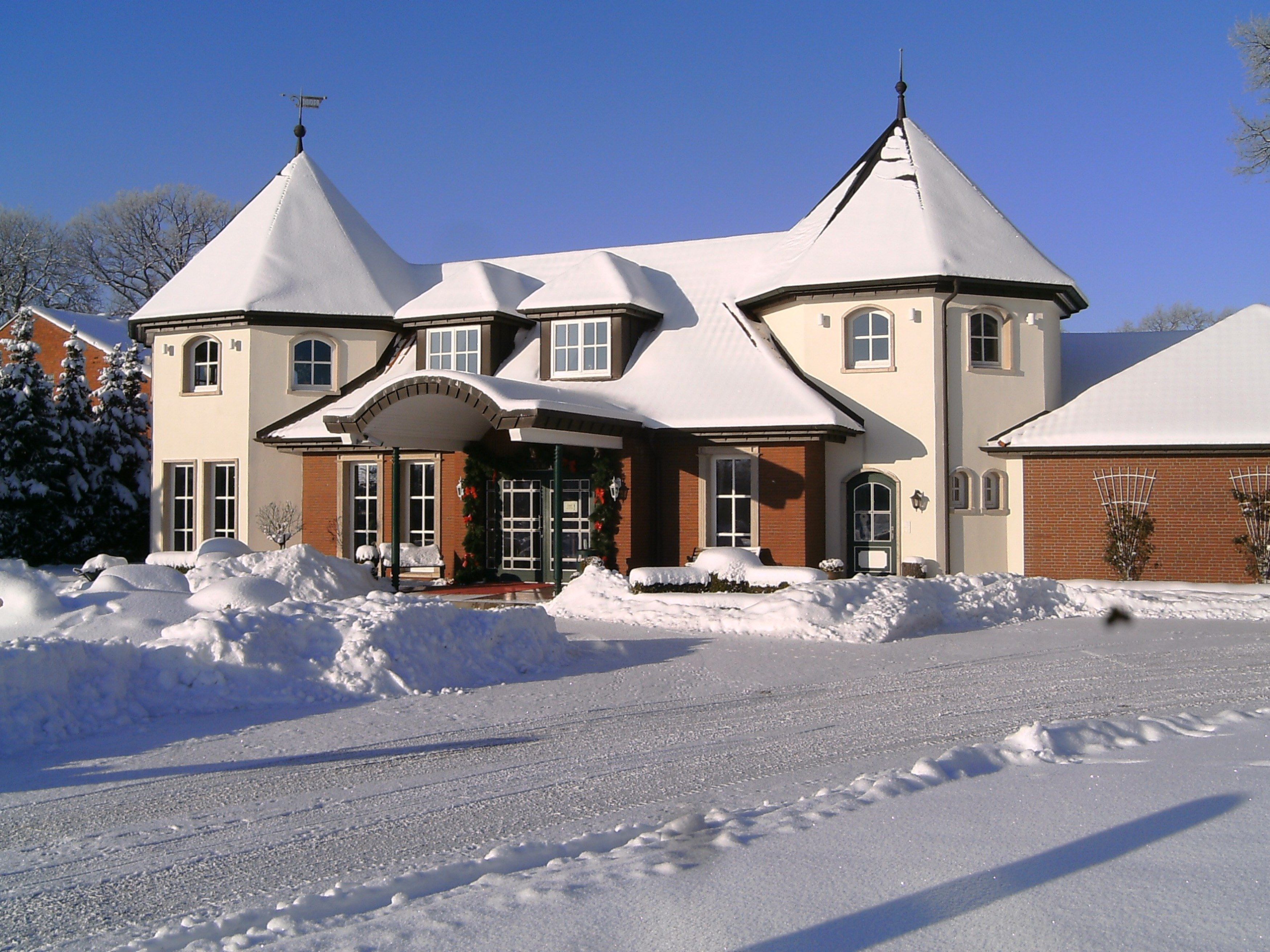 A large, multi-story building with a symmetrical facade, multiple windows, and a central entrance with a covered porch. Snow is piled in front of the building, and there are visible tracks on the snow-covered ground.