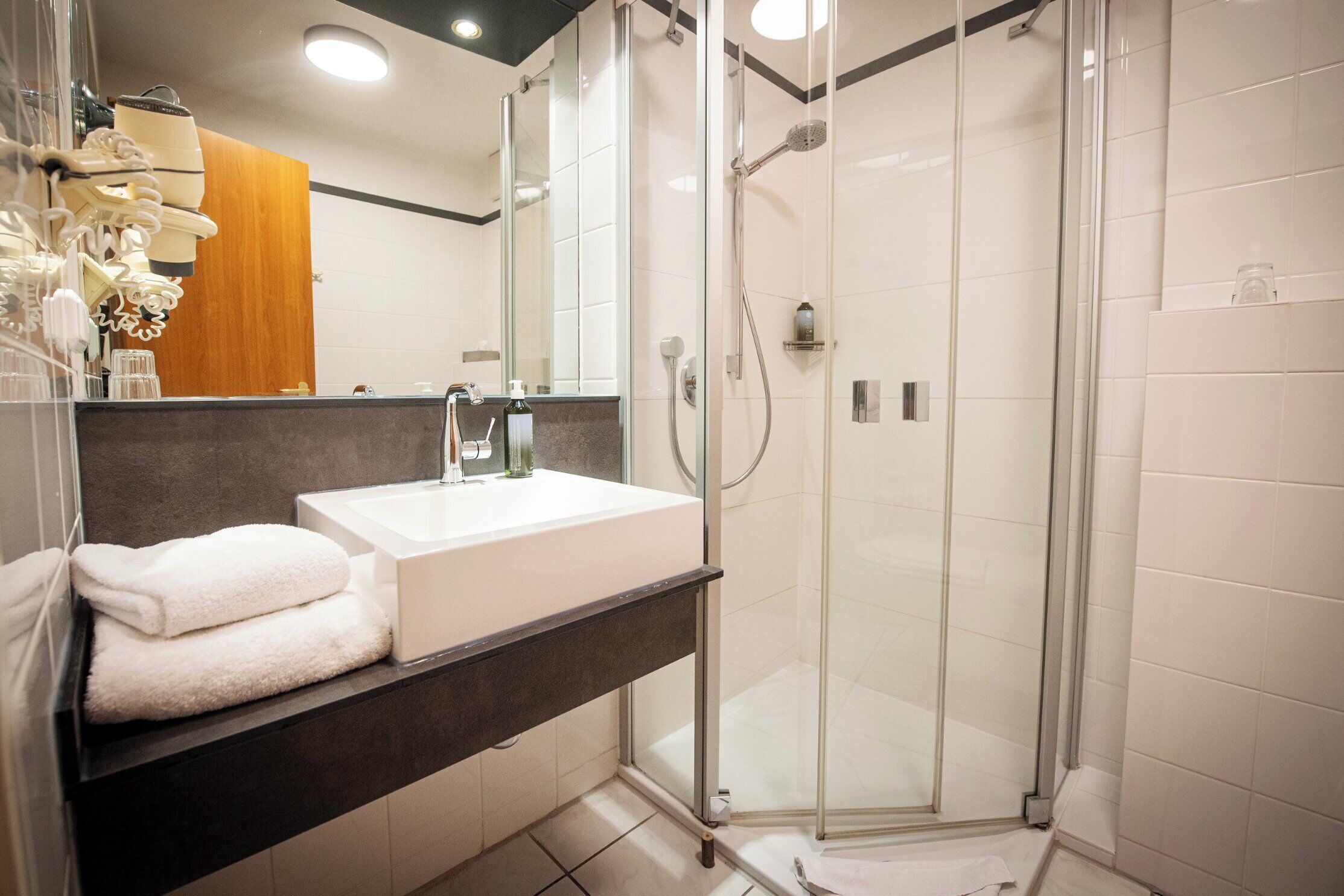 Un baño moderno con cabina de ducha de vidrio, un lavabo blanco y una encimera oscura.