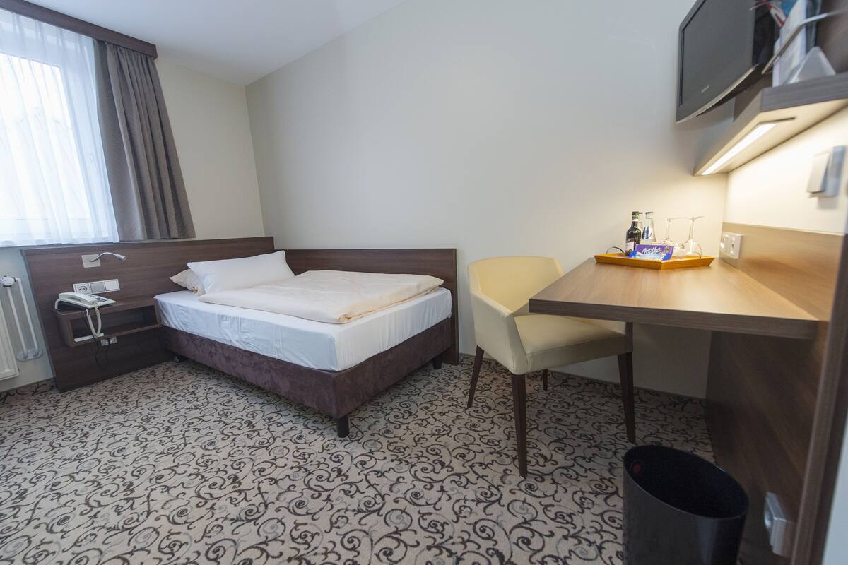 A hotel room with a bed, a desk, a chair, a television, and a window with curtains.