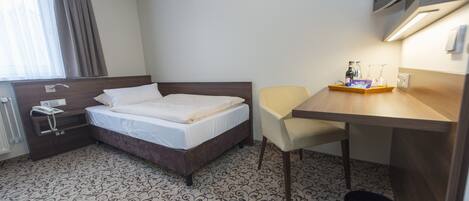 Una habitación de hotel con cama, escritorio, silla, televisor y ventana con cortinas.