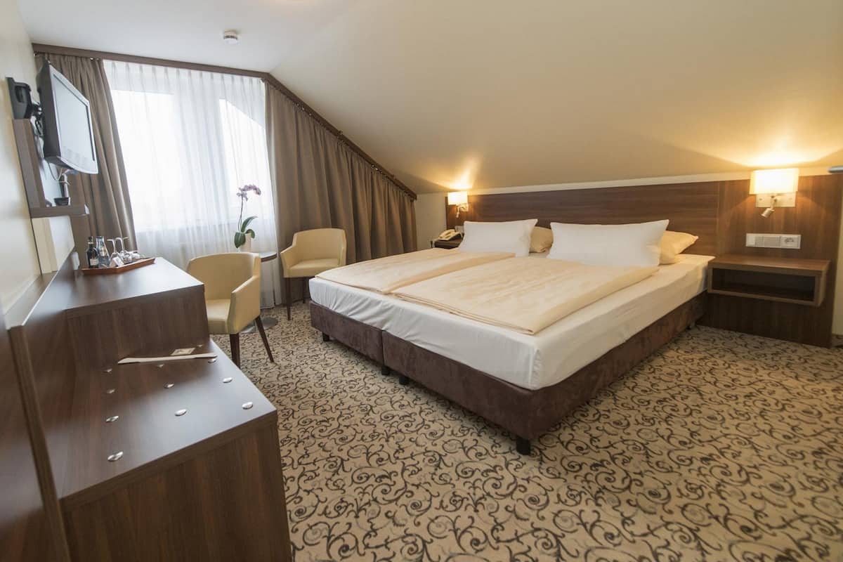 A hotel room with a large bed, a desk with a chair, a TV, and a desk lamp.
