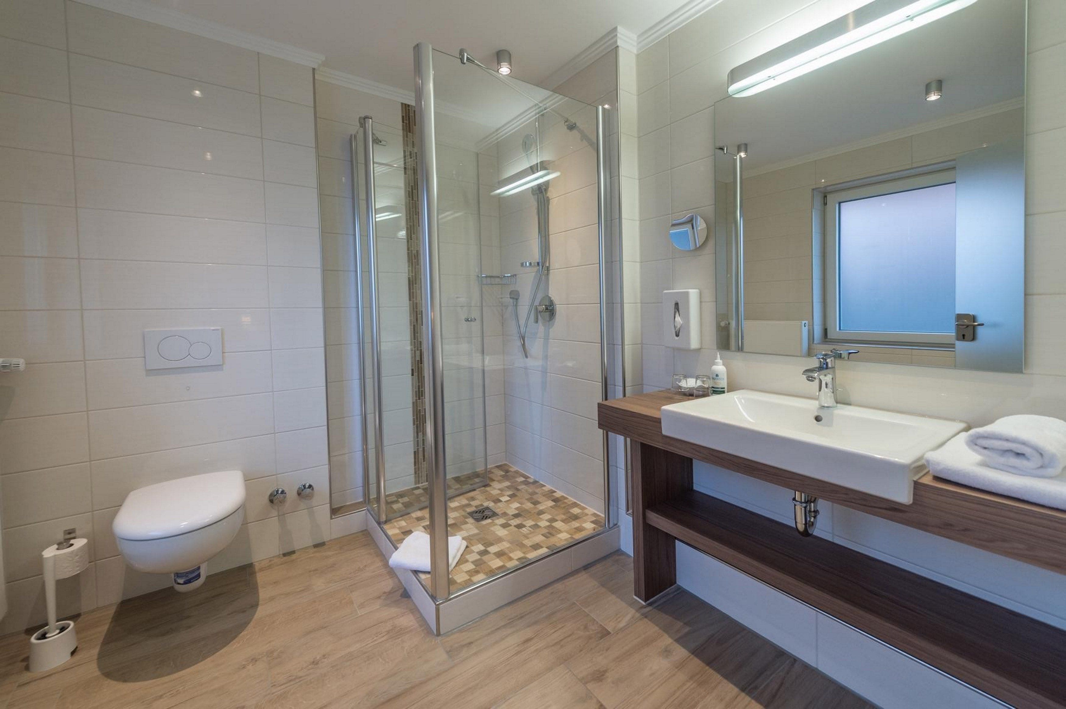 Een moderne badkamer met een douchecabine van glas, een wit toilet en een houten wastafelmeubel met een wastafel.