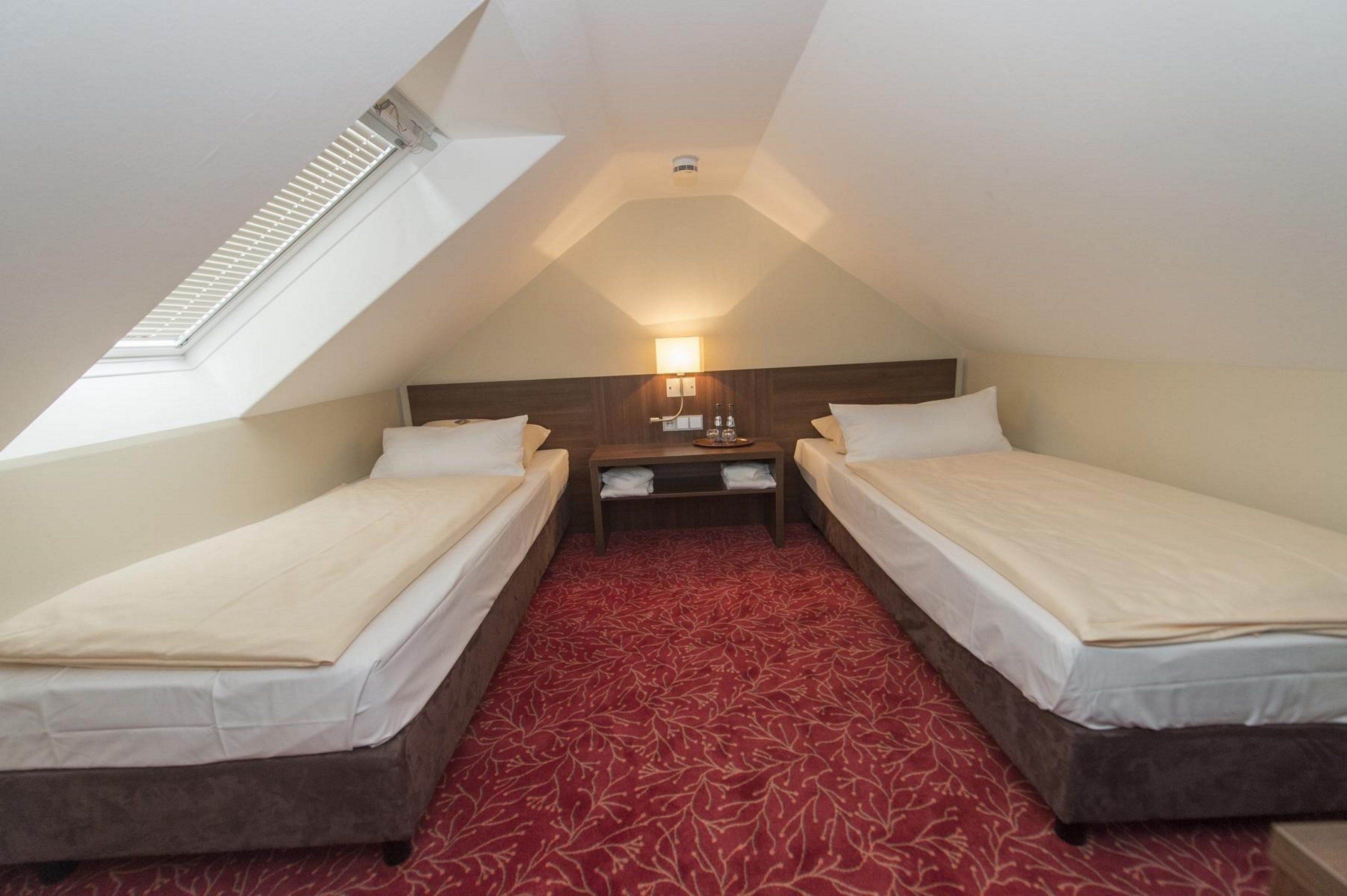 A small, triangular attic bedroom with two single beds, a nightstand, and a skylight.
